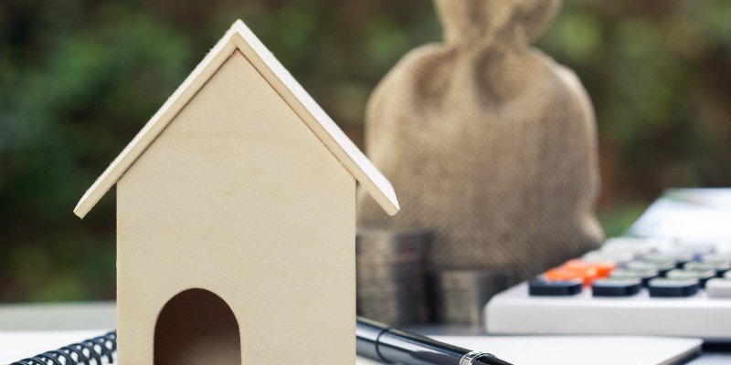 mini wooden house with calculator and money bag behind it